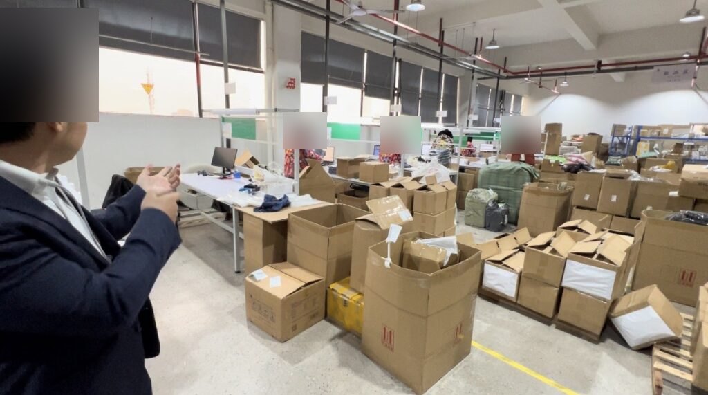ラクマートの検品エリア。検品台の奥にスタッフが並び、手前に開梱された段ボールが置かれている様子