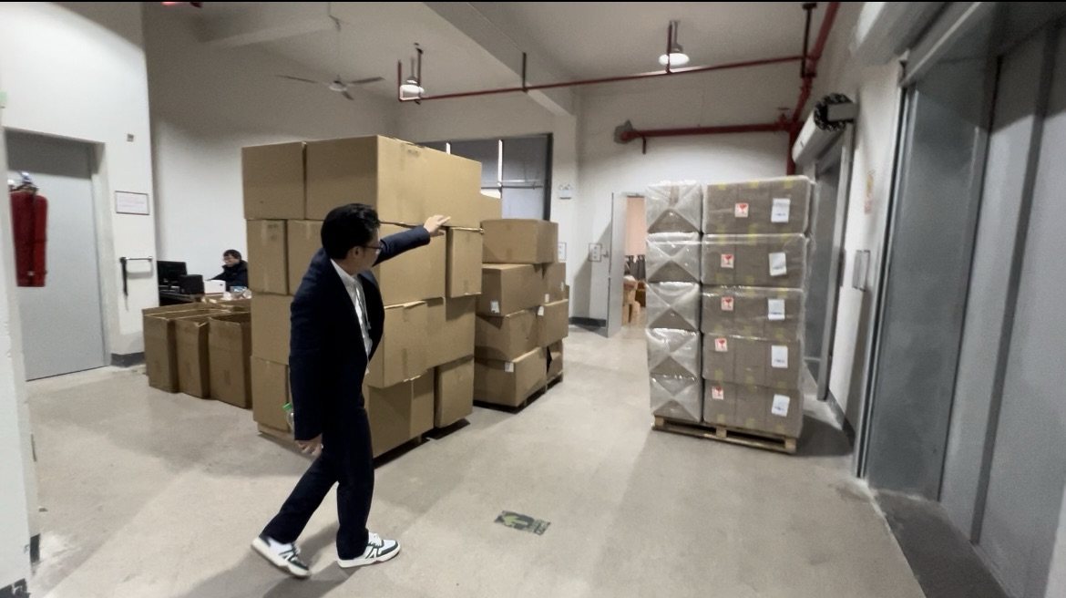 ラクマート本社の倉庫フロアに、中国の工場から届いた段ボールが積まれている様子。奥にエレベーターとラップ巻きのパレット